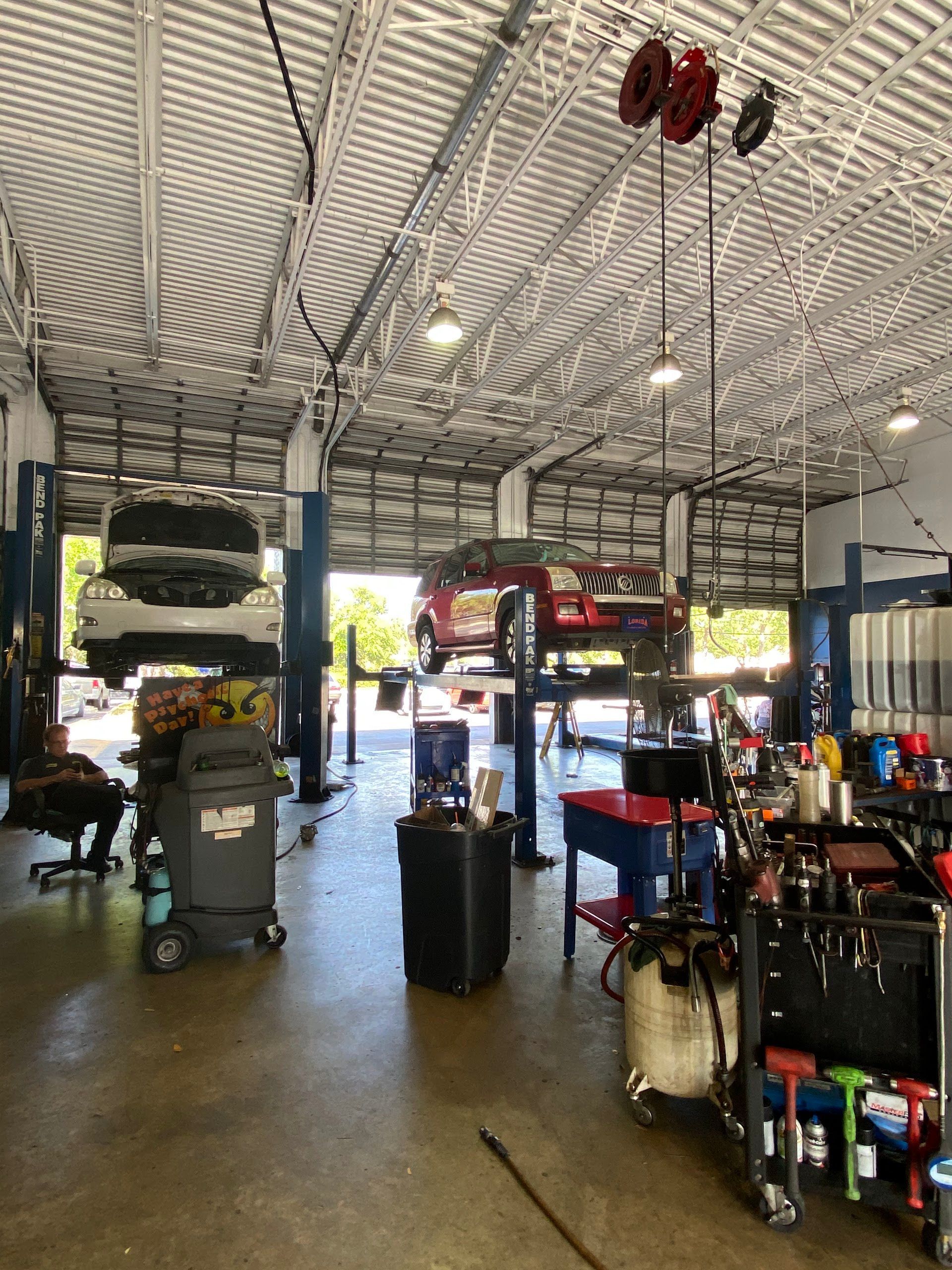 Inside a car repair shop with vehicles on lifts. Tools, equipment, and open garage doors are visible. | Brake World