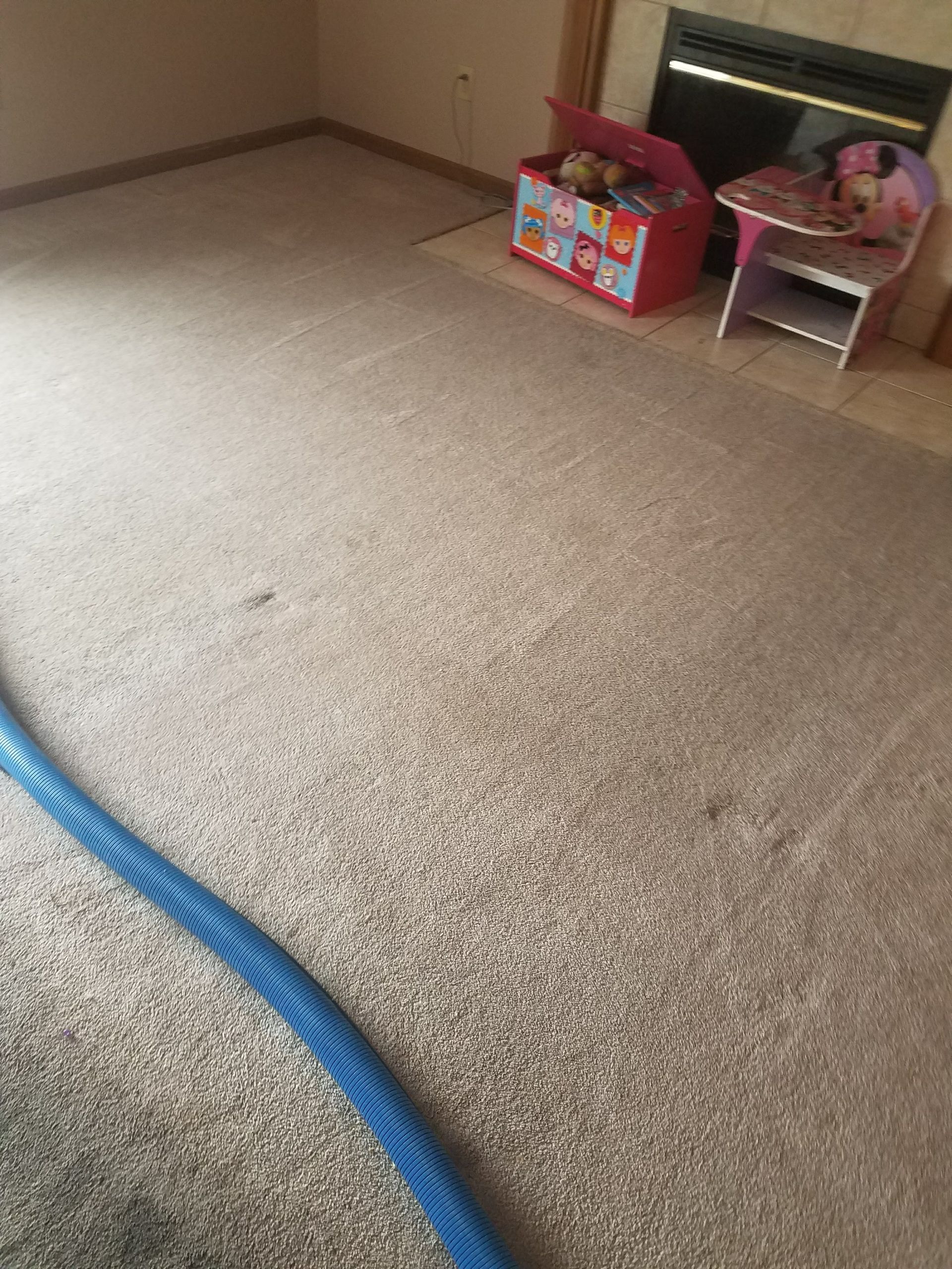 A living room with a fireplace and a box of toys on the floor.