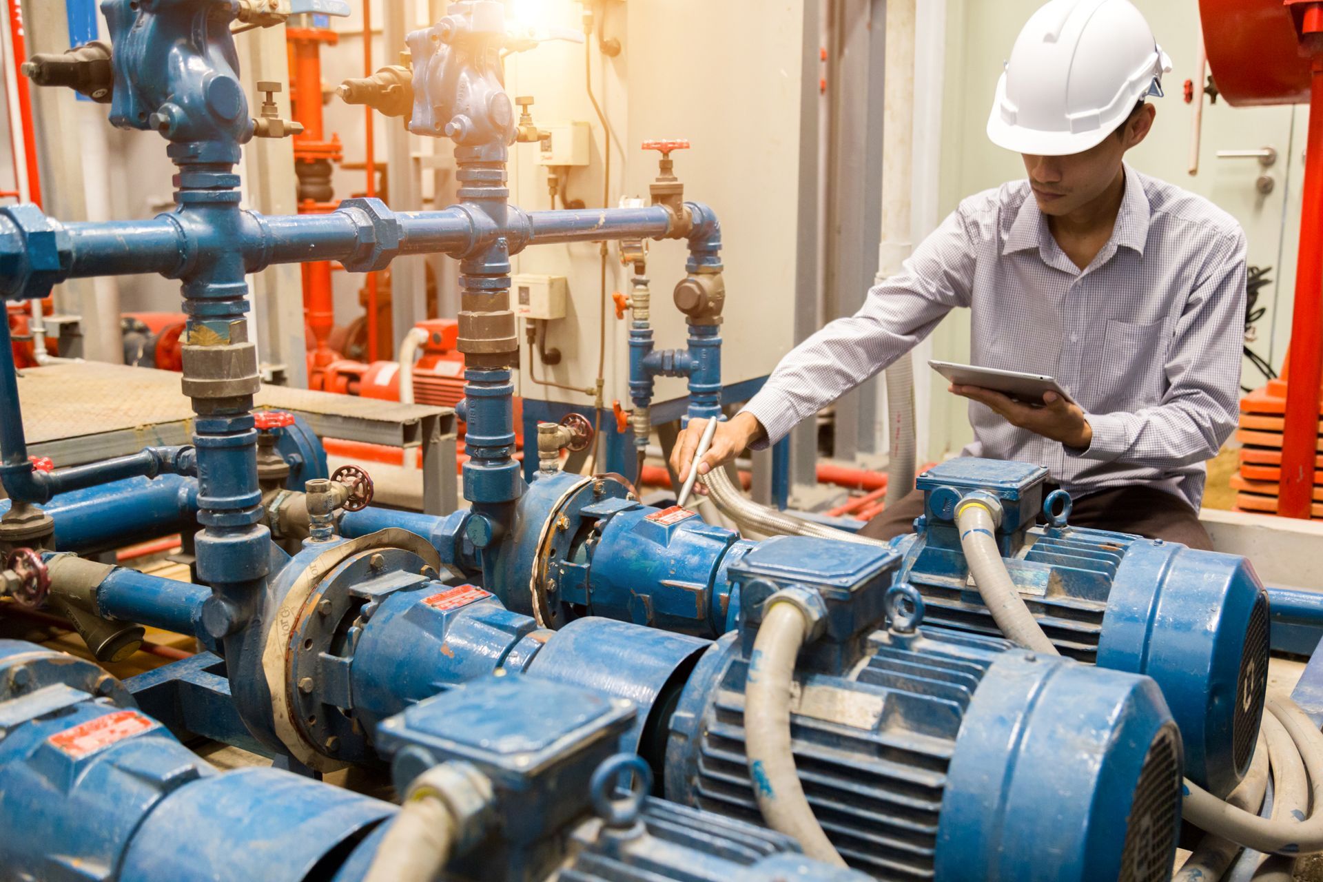 Technician with tablet inspecting blue industrial pumps and piping for pump systems sales