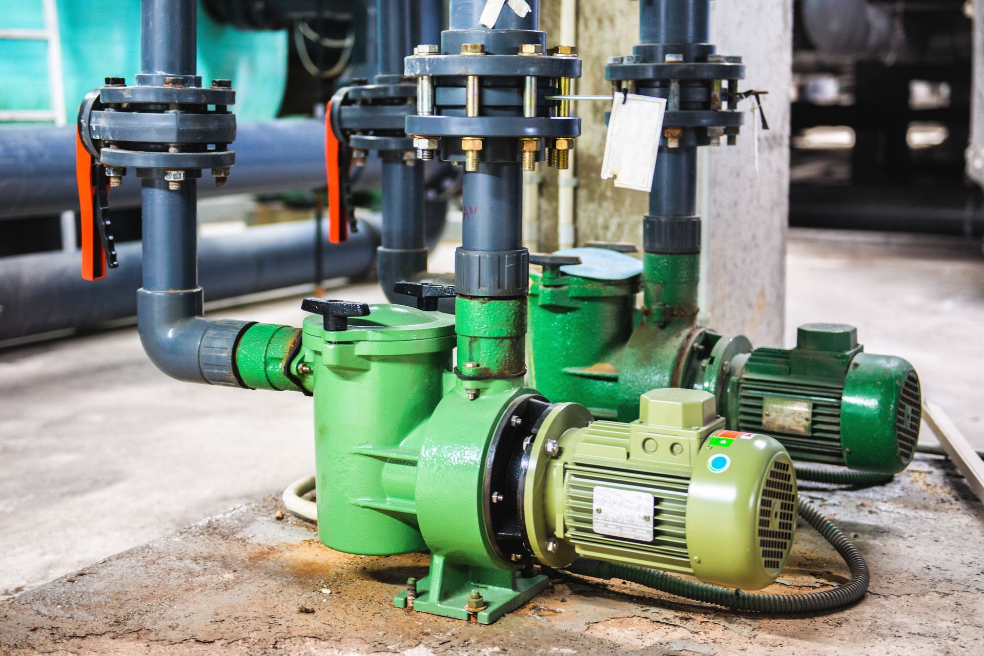 A green pump is sitting next to a bunch of pipes.