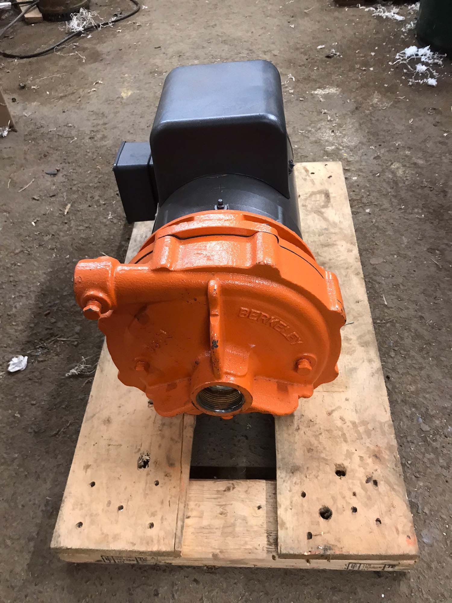 An orange and black motor is sitting on top of a wooden pallet.