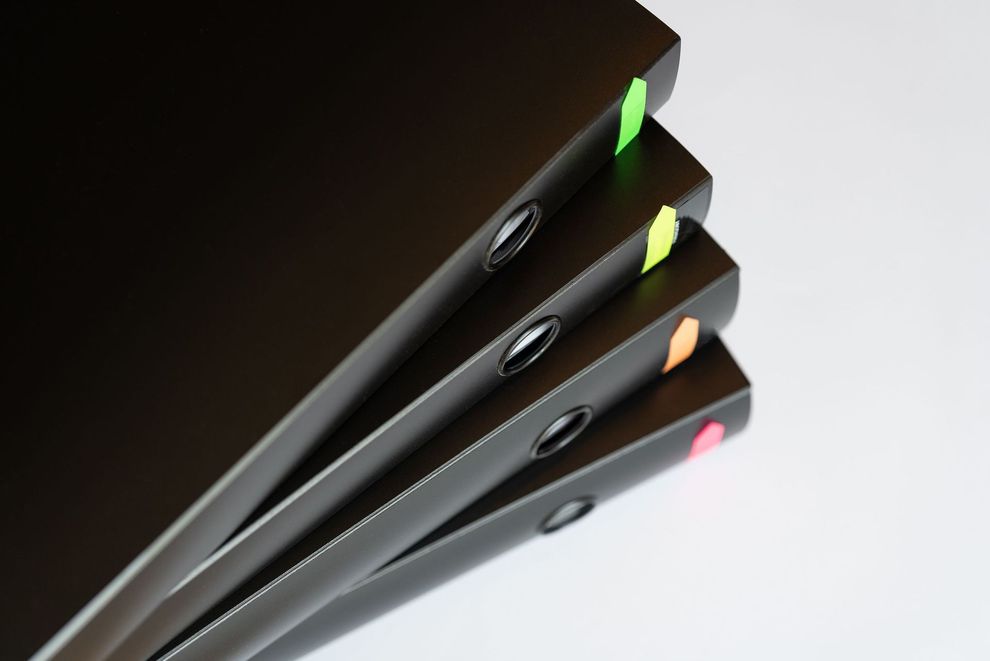 Pila di eleganti quaderni neri con segnalibri colorati su sfondo bianco.