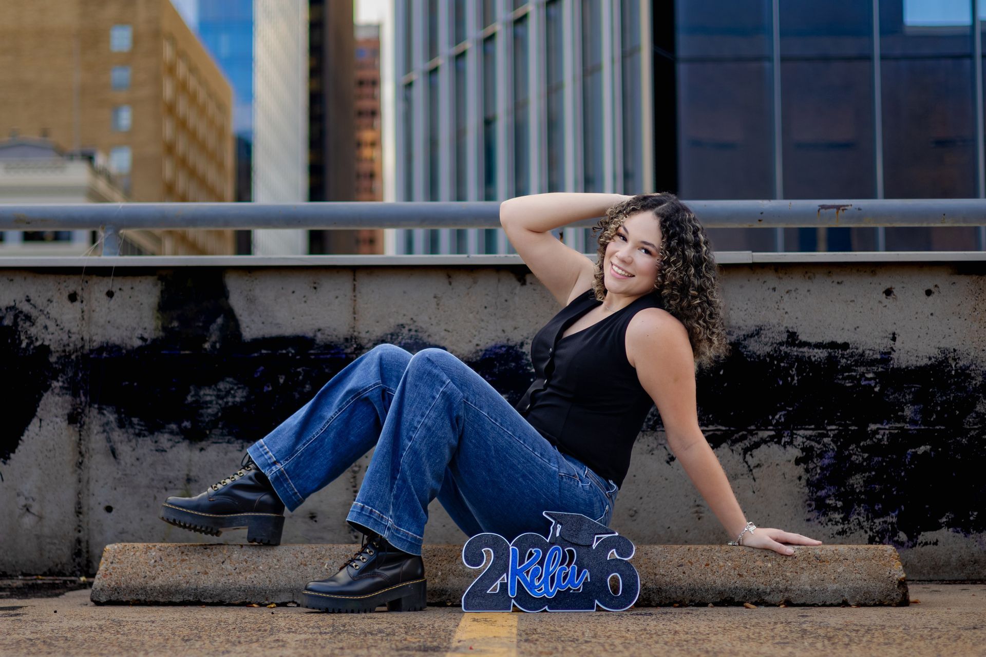 High school senior sitting on an urban rooftop during a senior photo session, smiling naturally with