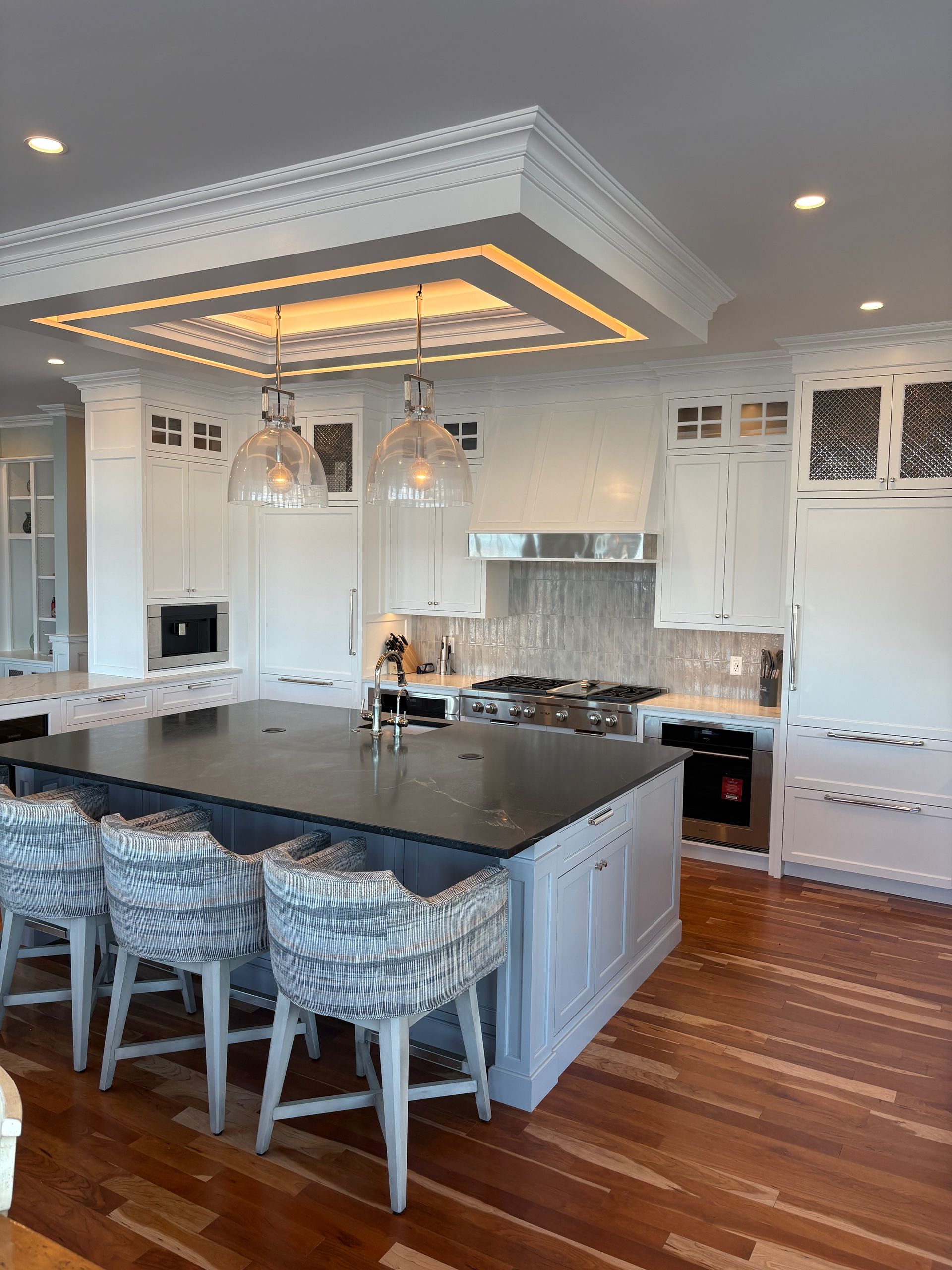 Kitchen with large island, white cabinets, dark countertop, and decorative ceiling.