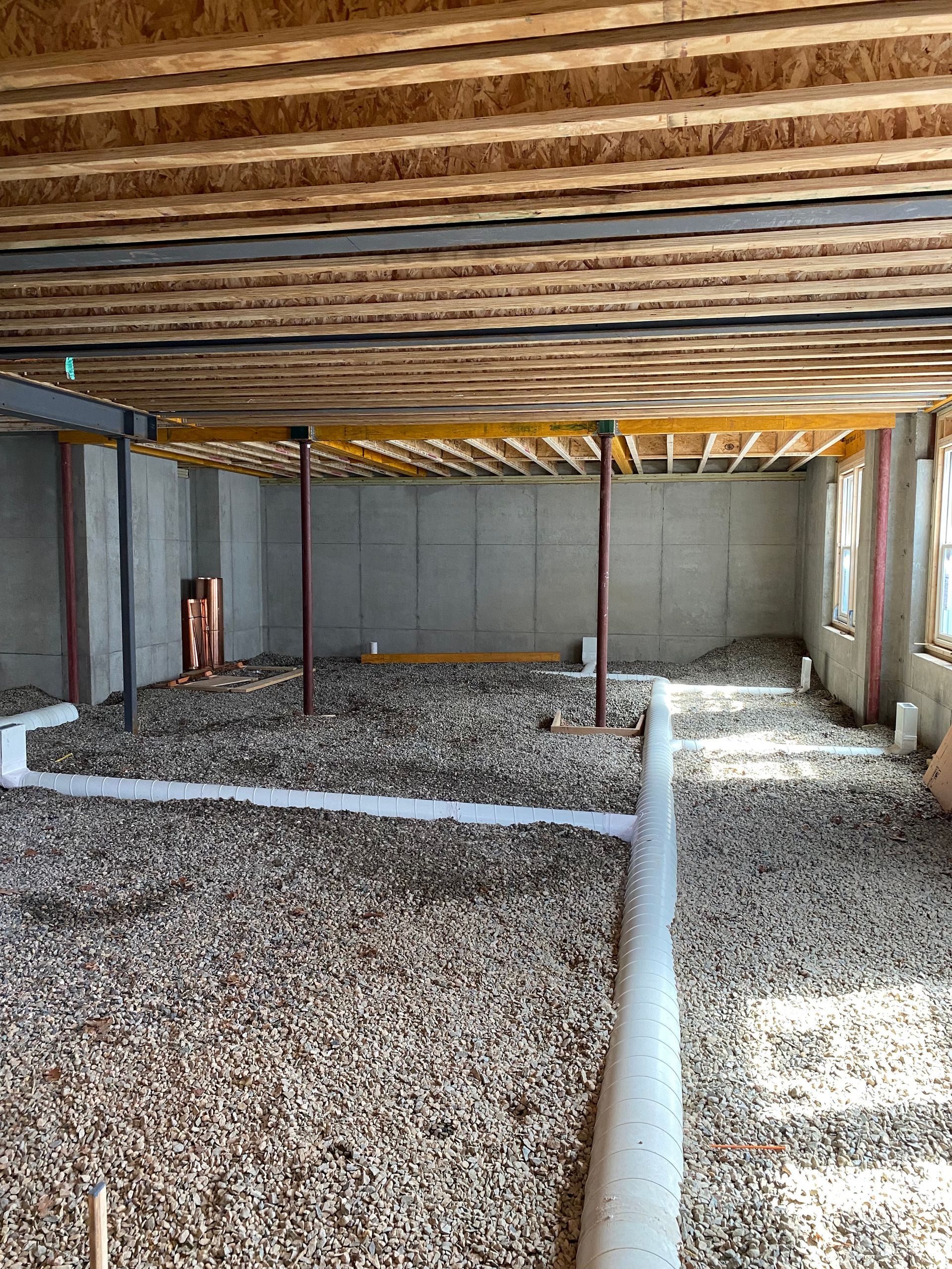 Interior of a building under construction. Brown gravel floor, support columns, and exposed wooden ceiling beams.