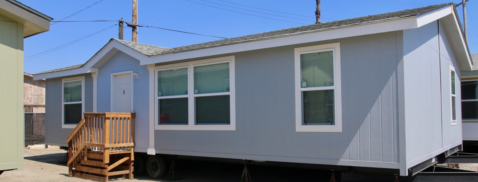 A light blue manufactured home with a wooden porch and white-framed windows on a sunny day.