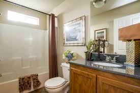 Bathroom with brown vanity, toilet, white tub, and artwork.