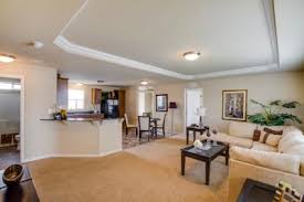 Open-concept living space with beige walls, a brown carpet, and a light-colored couch. Kitchen and dining area visible.