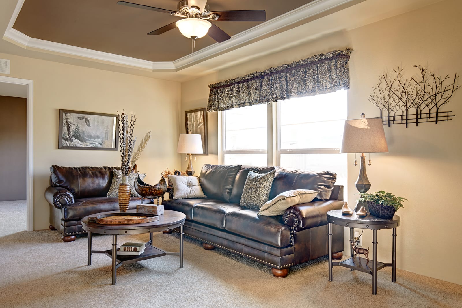 Living room with brown leather furniture, coffee tables, and a window with a valance.