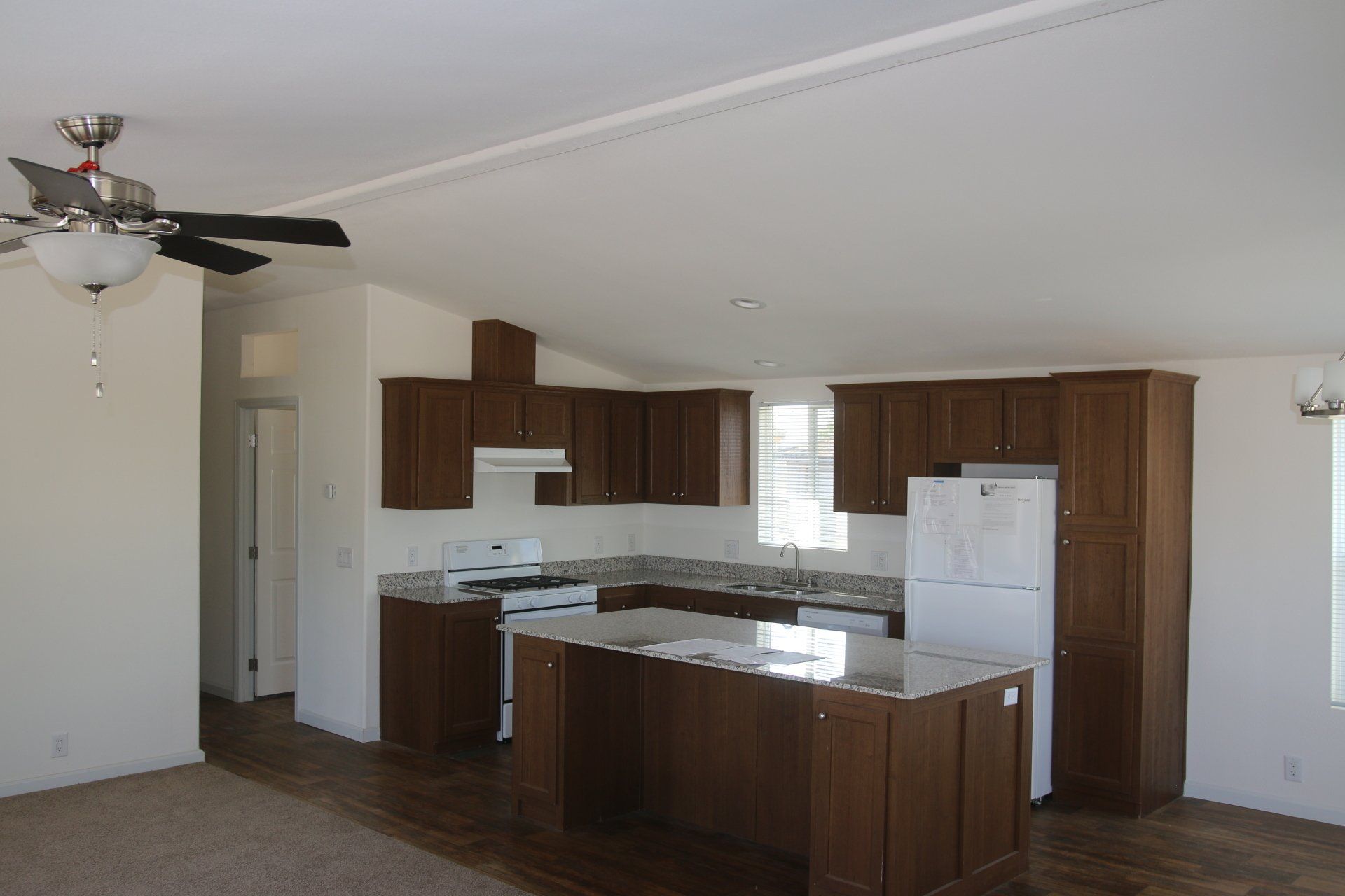 Interior of a kitchen with dark cabinets, a white refrigerator, and a kitchen island with granite countertop.