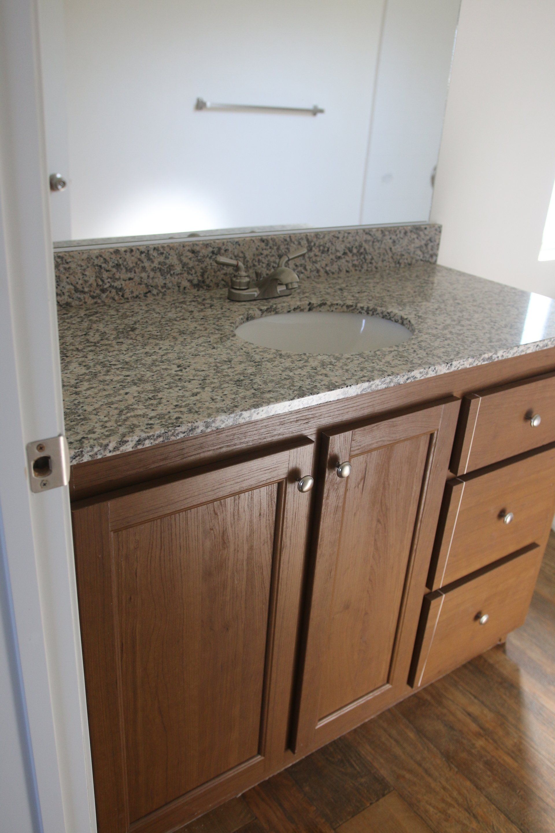 Bathroom vanity with a granite countertop, wood cabinets, and a sink.
