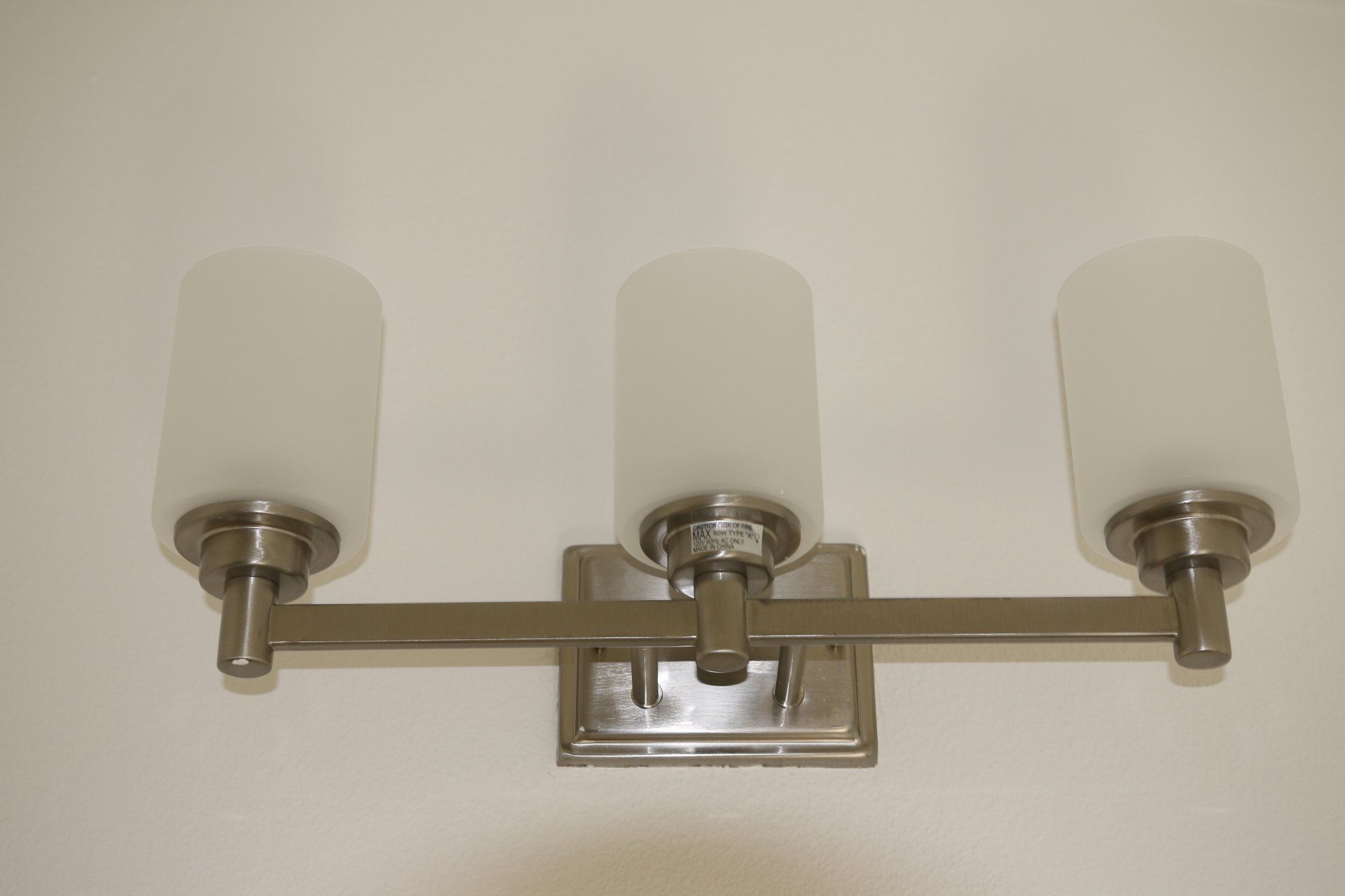 Three-light bathroom vanity fixture with frosted cylindrical shades, mounted on a white wall.