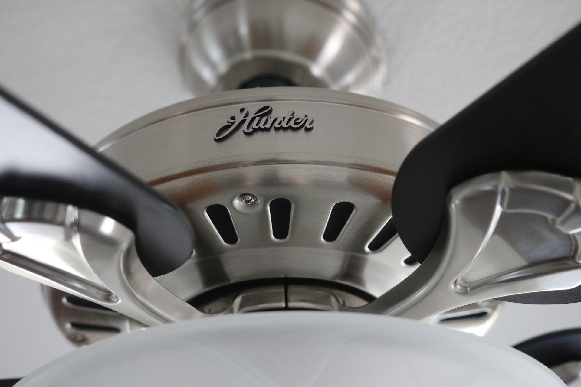 Close-up of a Hunter ceiling fan with silver finish, black blades, and a white light fixture.