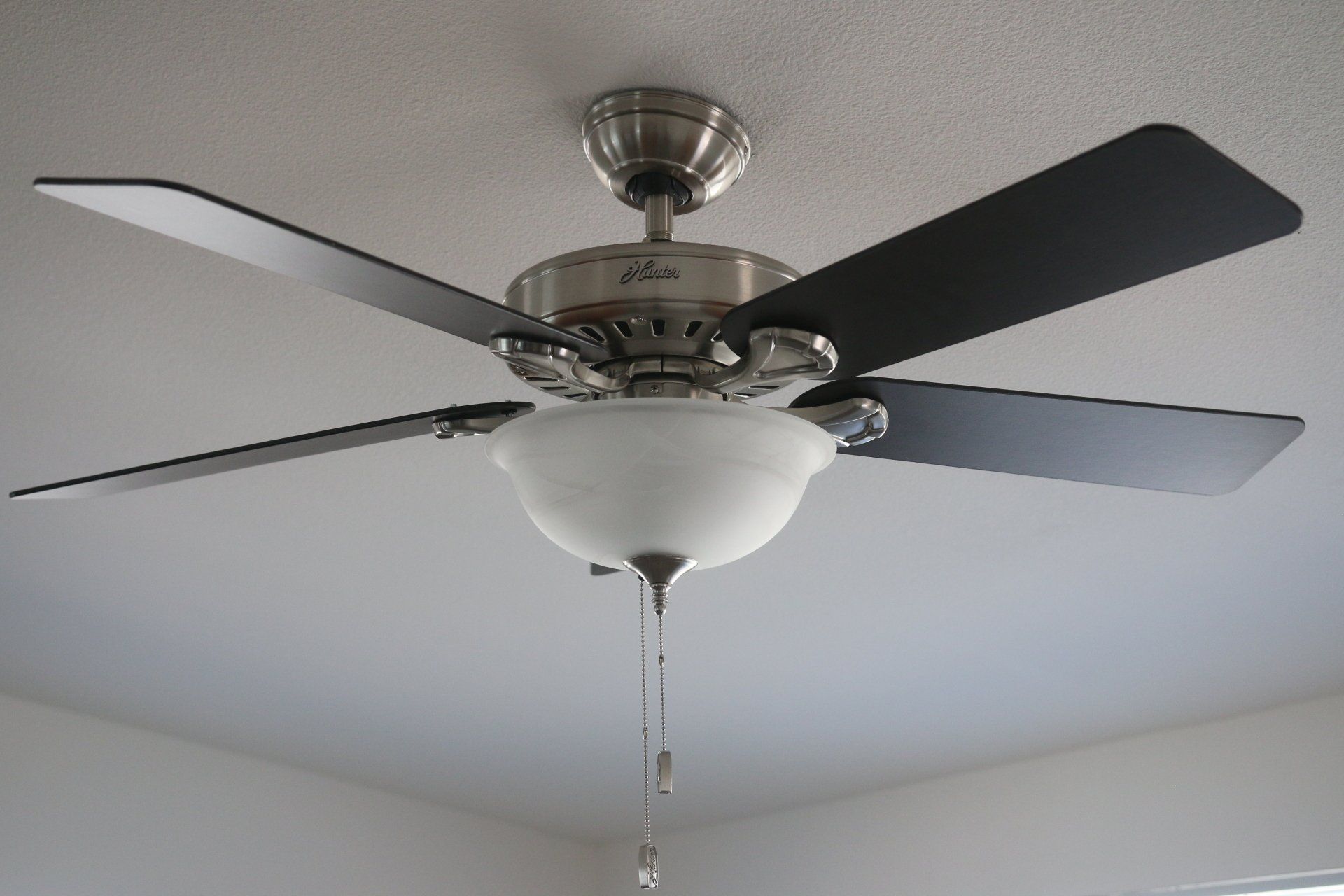 Ceiling fan with five black blades and a white glass light fixture.