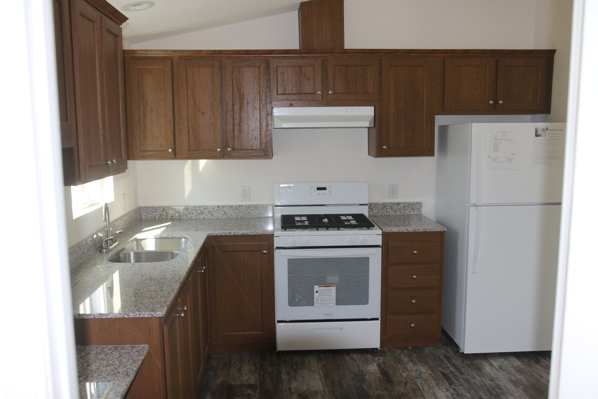 Kitchen with brown cabinets, white appliances, granite countertops, and dark flooring.