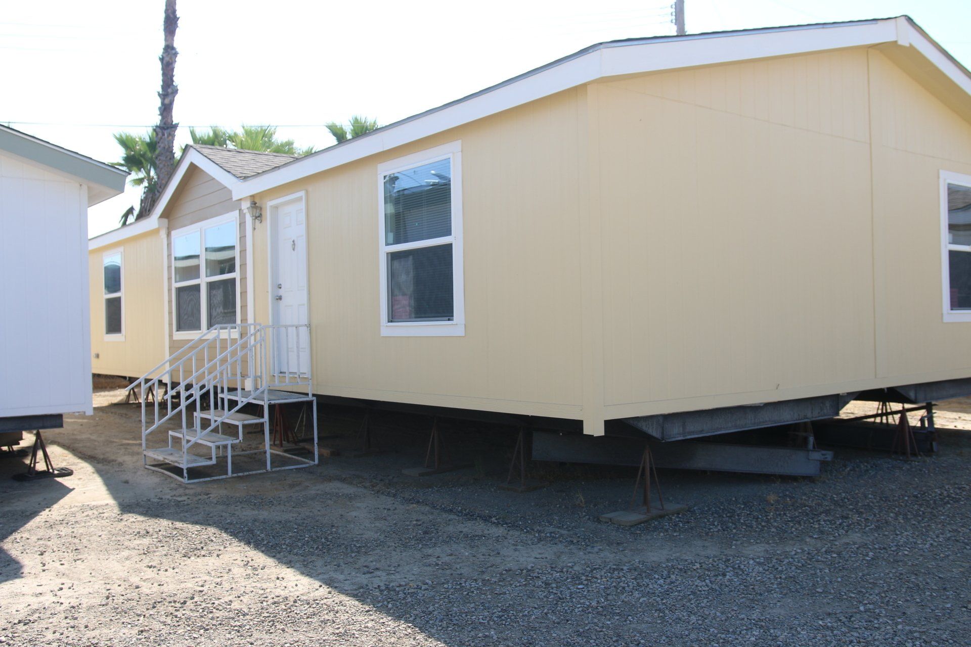 Light yellow mobile home with white trim and a small set of stairs, parked on gravel.