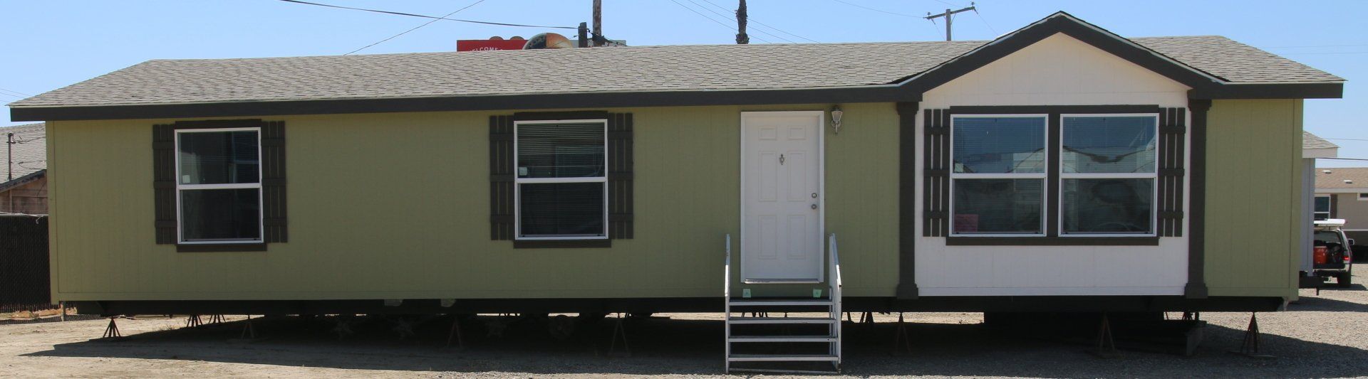 A light-green mobile home with a white door and windows. It's set on a gravel lot.