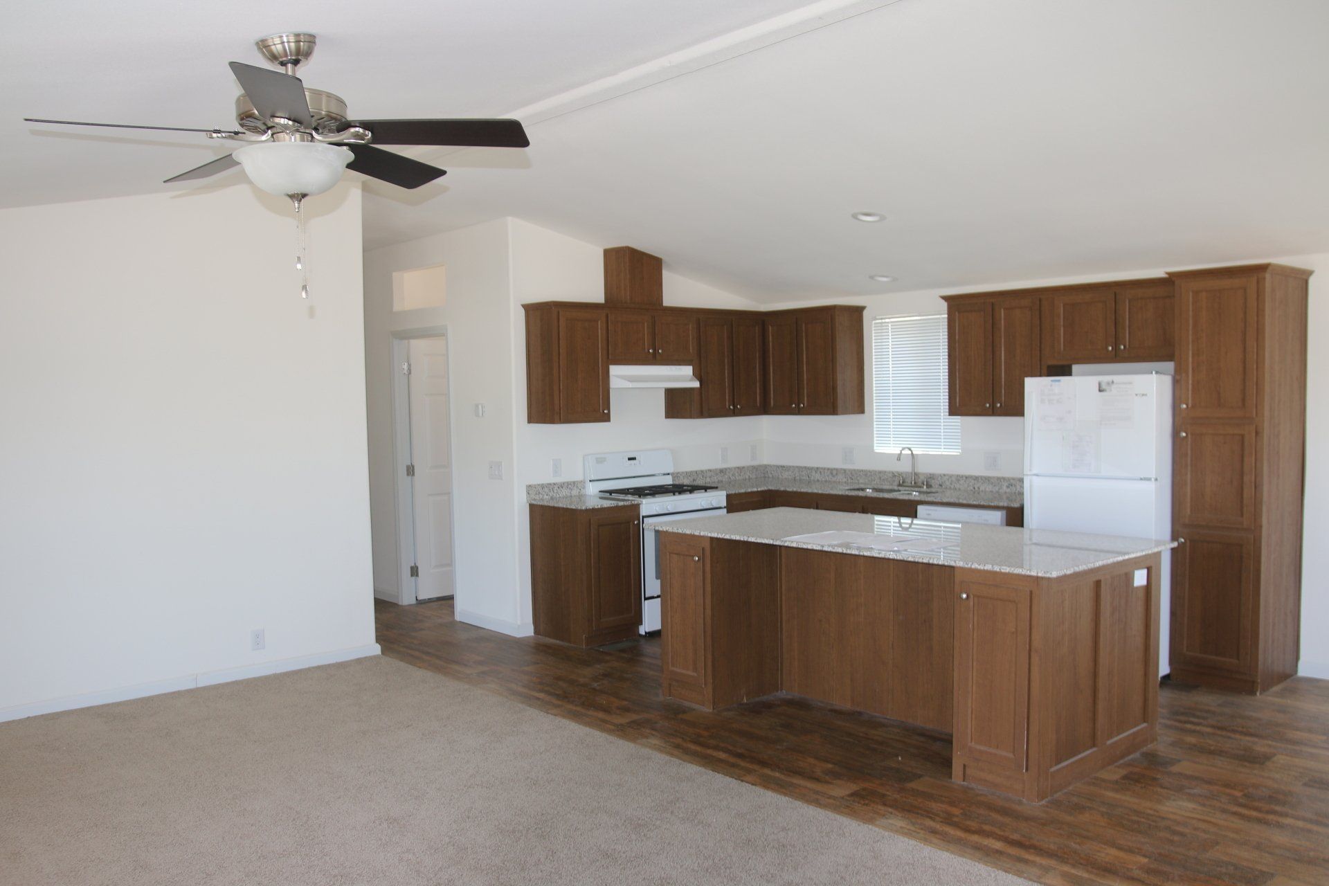 Open-concept kitchen with brown cabinets, island, white appliances, and a ceiling fan.