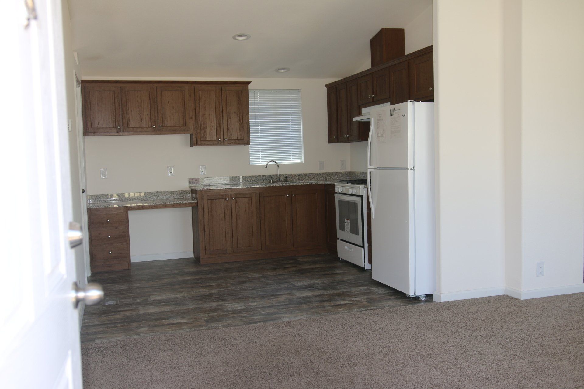 Interior view of a kitchen with brown cabinets, white appliances, and a window.