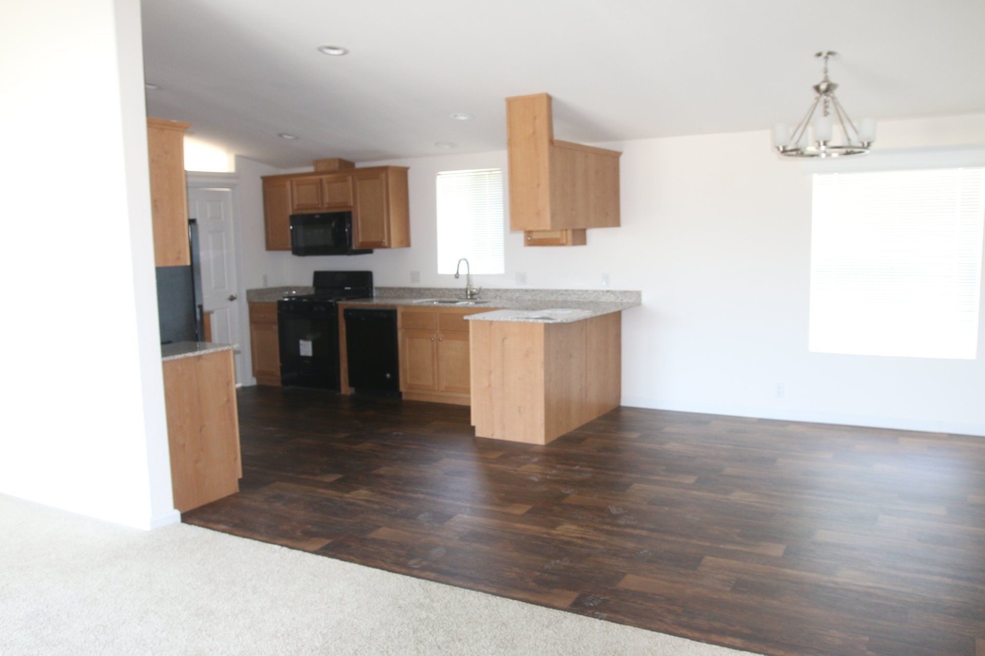Interior view of a kitchen with light wood cabinets, black appliances, and dark wood flooring.
