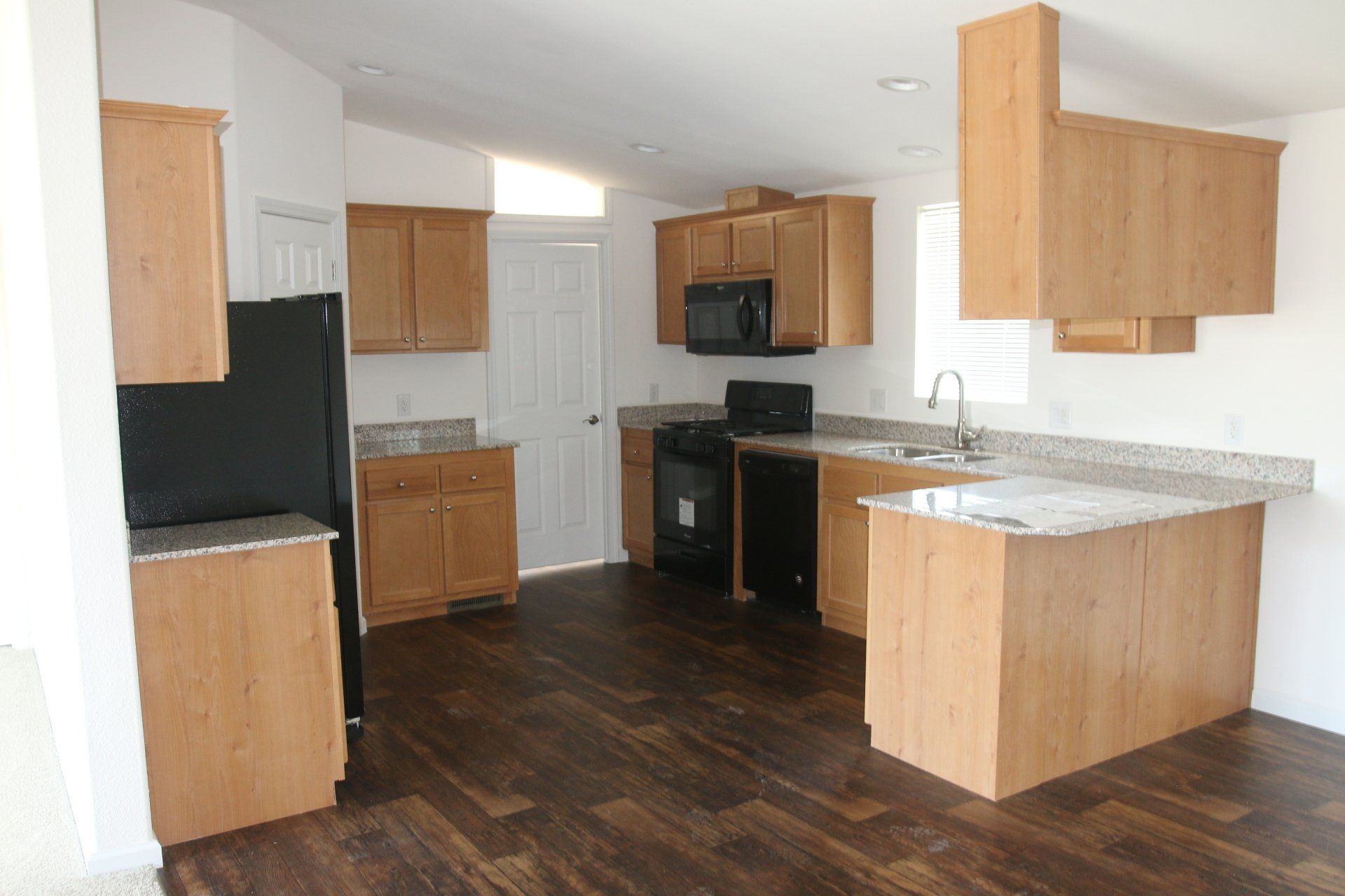 Kitchen with light wood cabinets, black appliances, granite countertops, and dark wood floors.