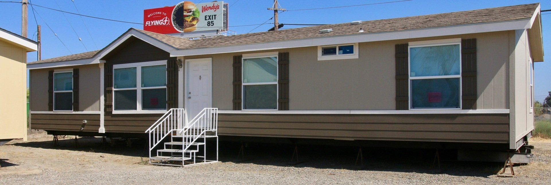 A tan and brown mobile home with white stairs on a sunny day.