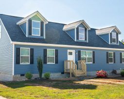 A blue house with a blue roof and black shutters is sitting on top of a lush green field.