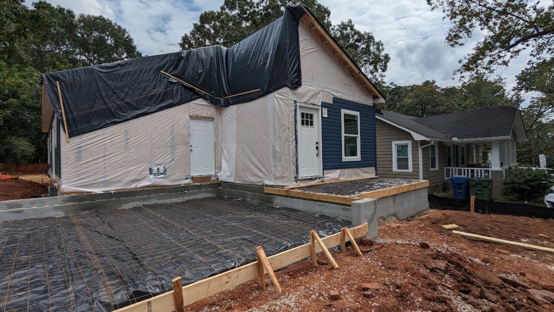Construction site. New house under construction, covered with tarp. Next to an existing house. Cloudy day.