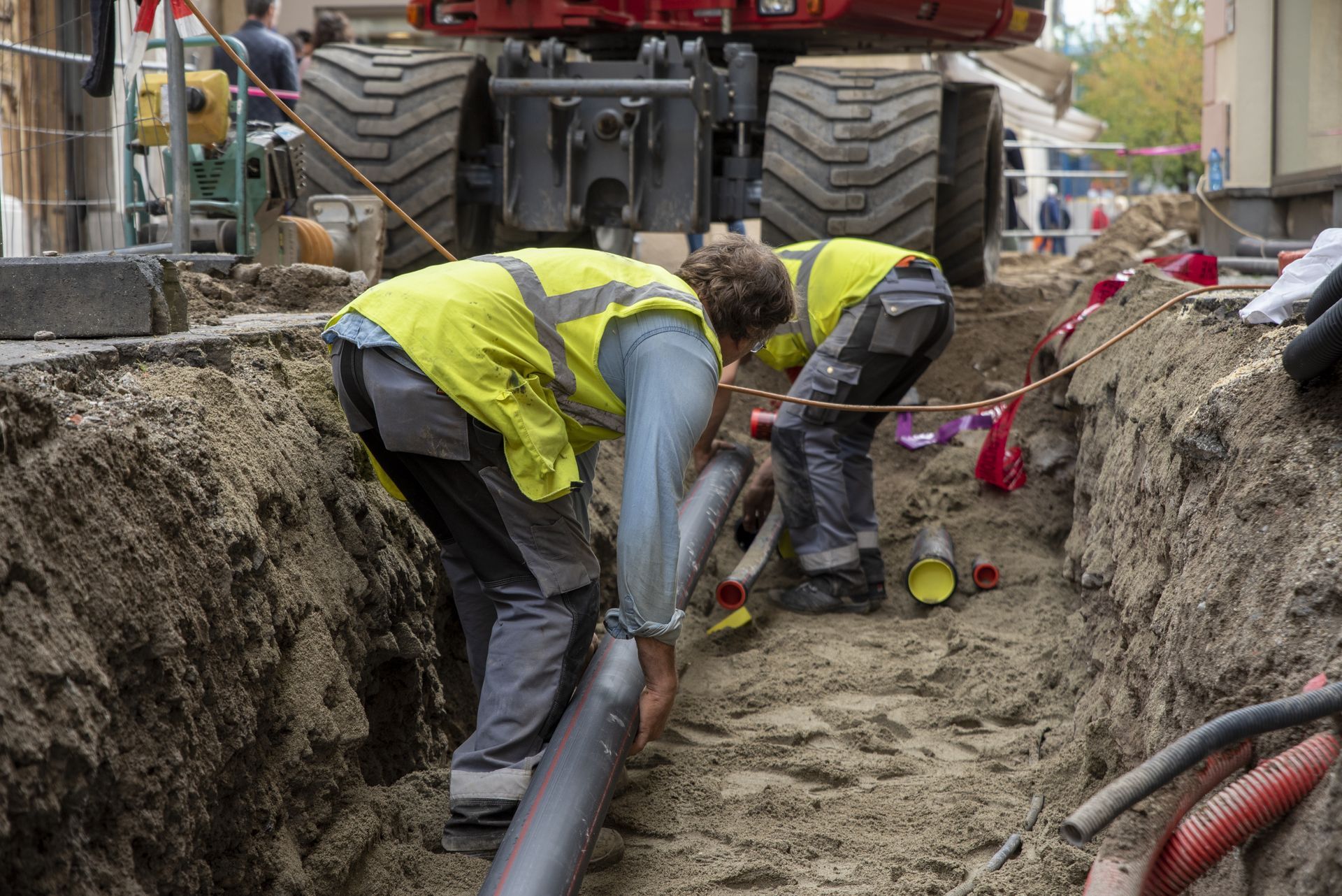 Construction workers laying a large pipe in a trench beside heavy machinery and dirt piles
