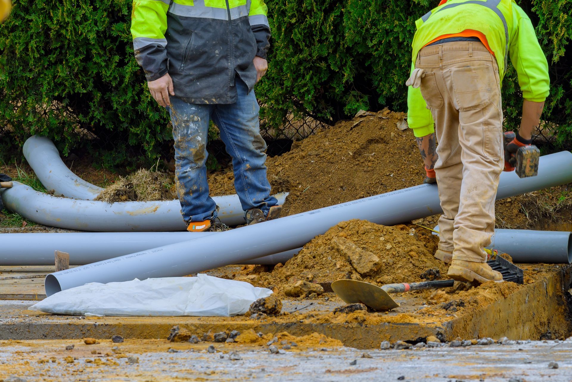 Workers handling large gray pipes at a muddy construction site