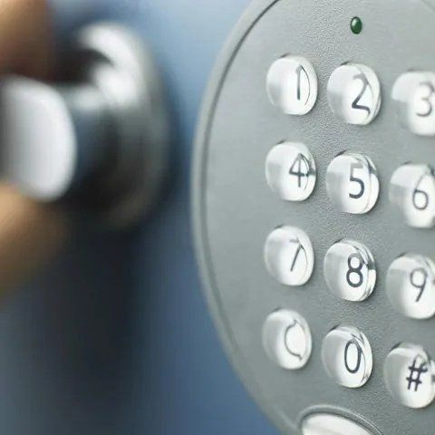 Primo piano di una tastiera di sicurezza grigia con tasti numerici bianchi e una manopola sfocata sullo sfondo.