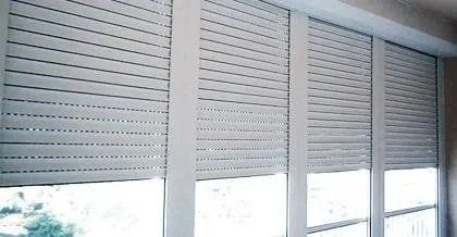 Tende a rullo bianche parzialmente chiuse su una finestra luminosa in una stanza