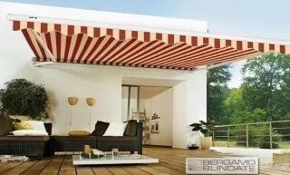 Patio moderno con tenda da sole a strisce rosse e bianche, posti a sedere all'aperto e vista su alberi verdi.