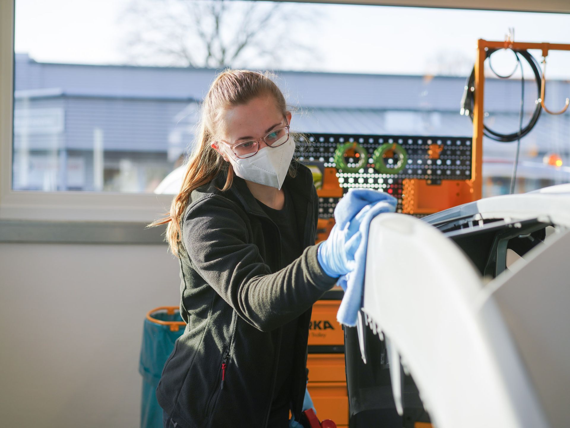 Eine Frau mit Maske und Handschuhen reinigt ein Auto mit einem Tuch.
