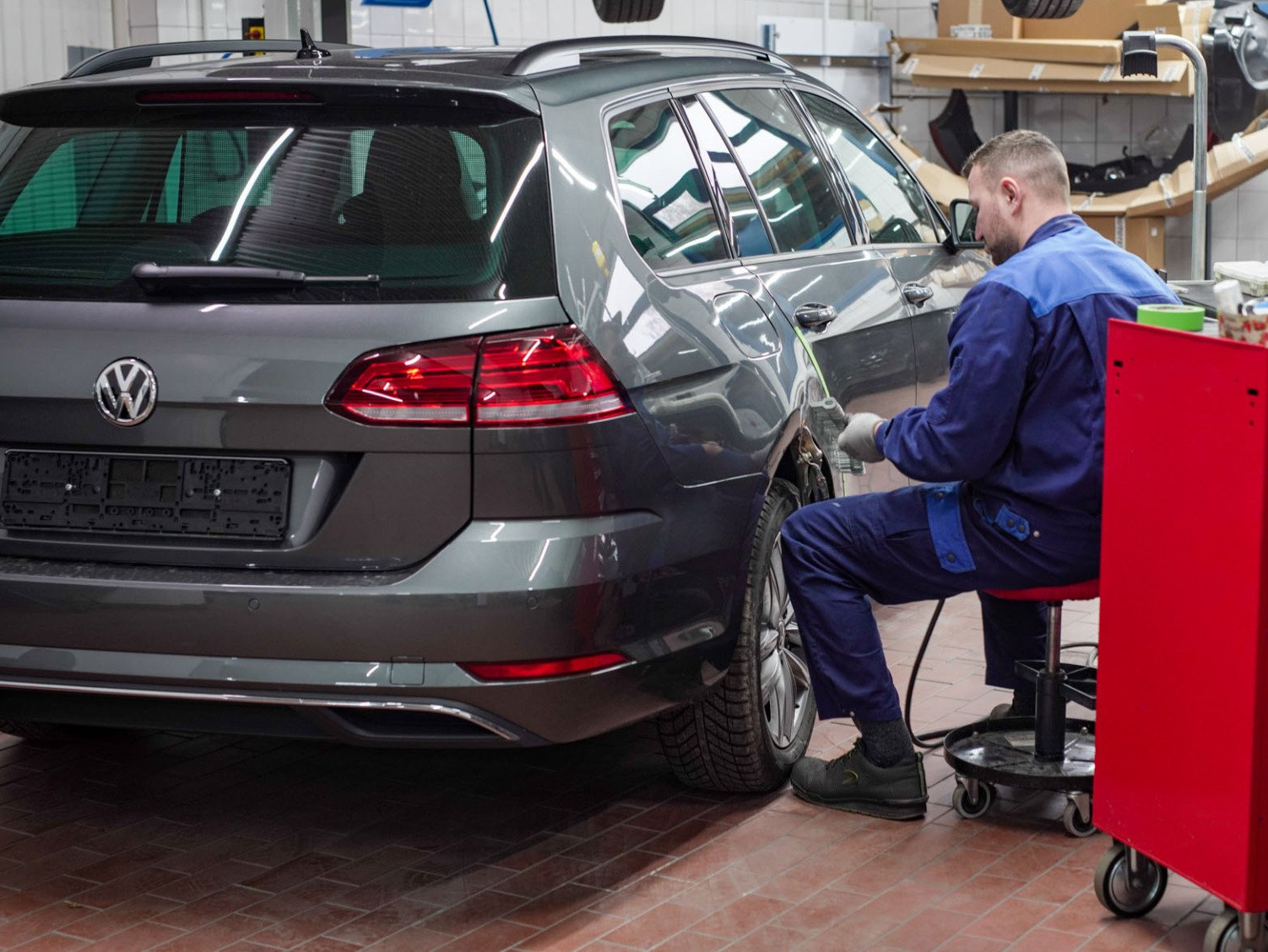 Ein Mann sitzt auf einem Hocker und arbeitet in einer Werkstatt an einem Auto.