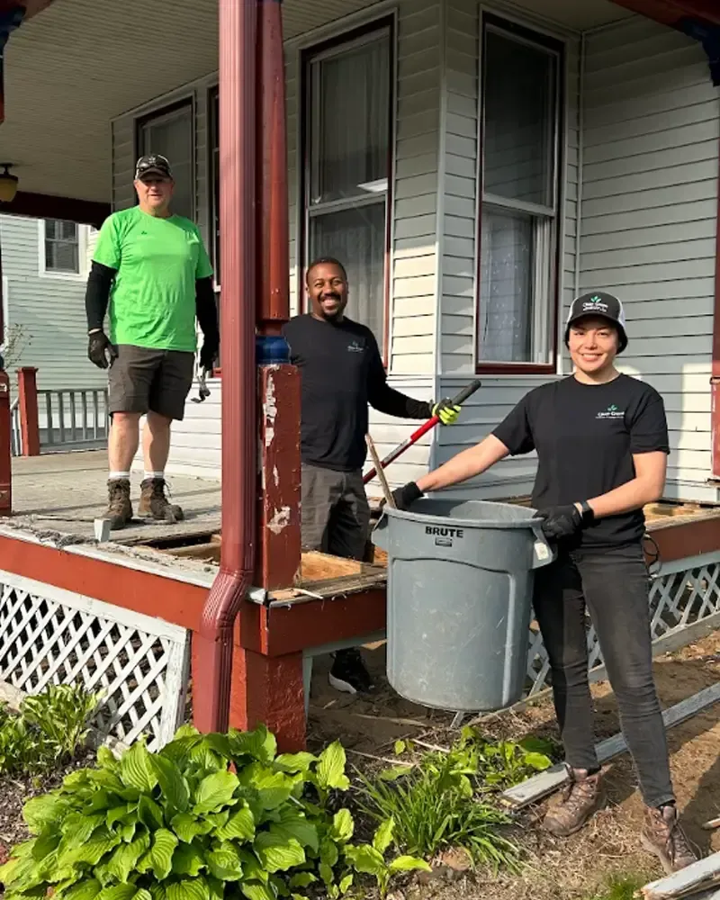 workers standing on a porch holding trash bags and tools during a cleanup.