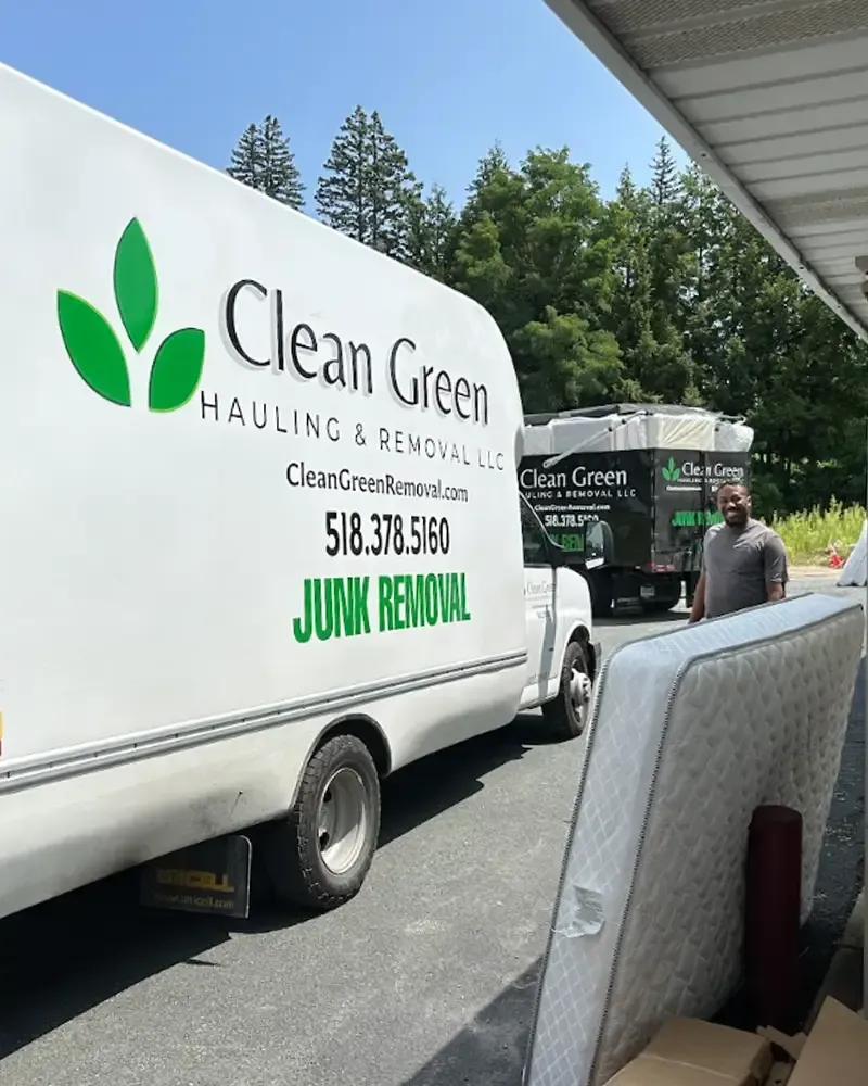 Clean Green Junk Removal truck parked outdoors beside a driveway, with a worker near the trailer.