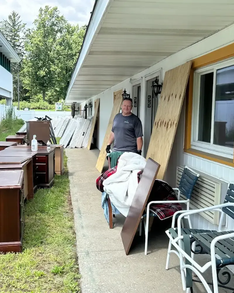 Person standing beside cluttered furniture and chairs on a covered porch walkway