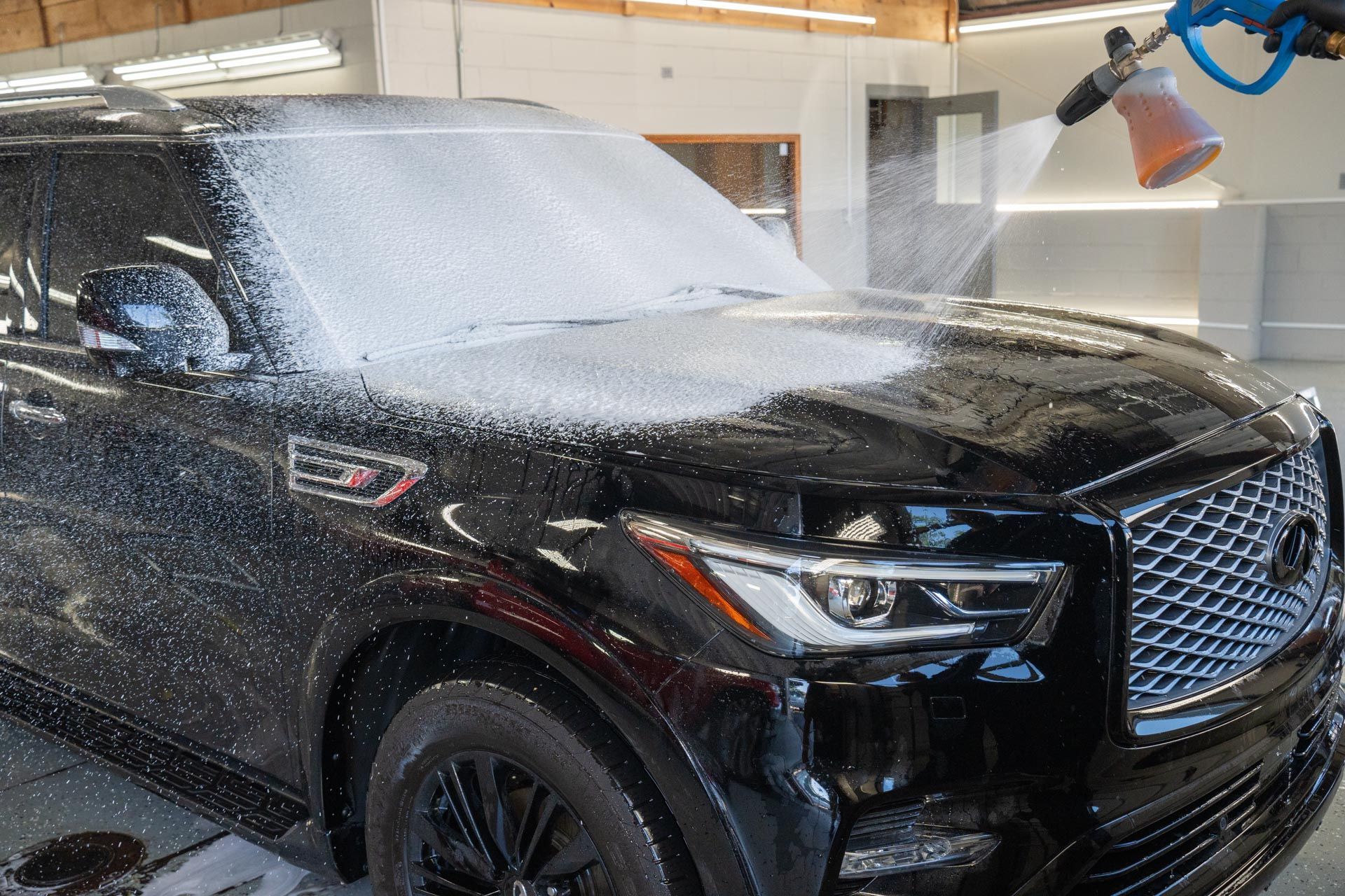 Black SUV being sprayed with foam in a car wash bay.