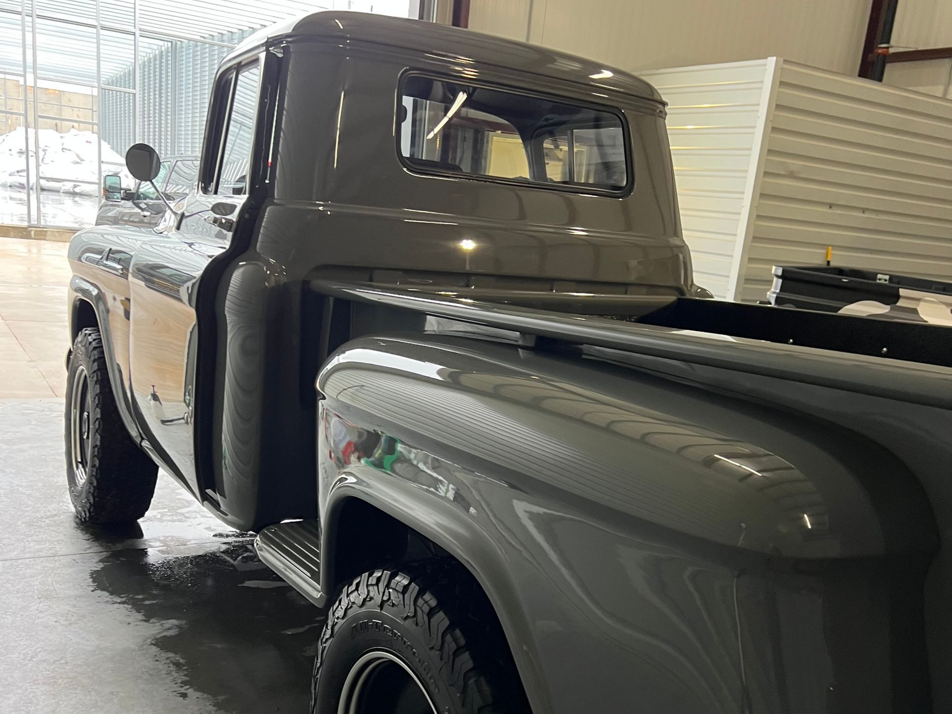 Gray vintage pickup truck with black tires parked near a building with snow visible outside.