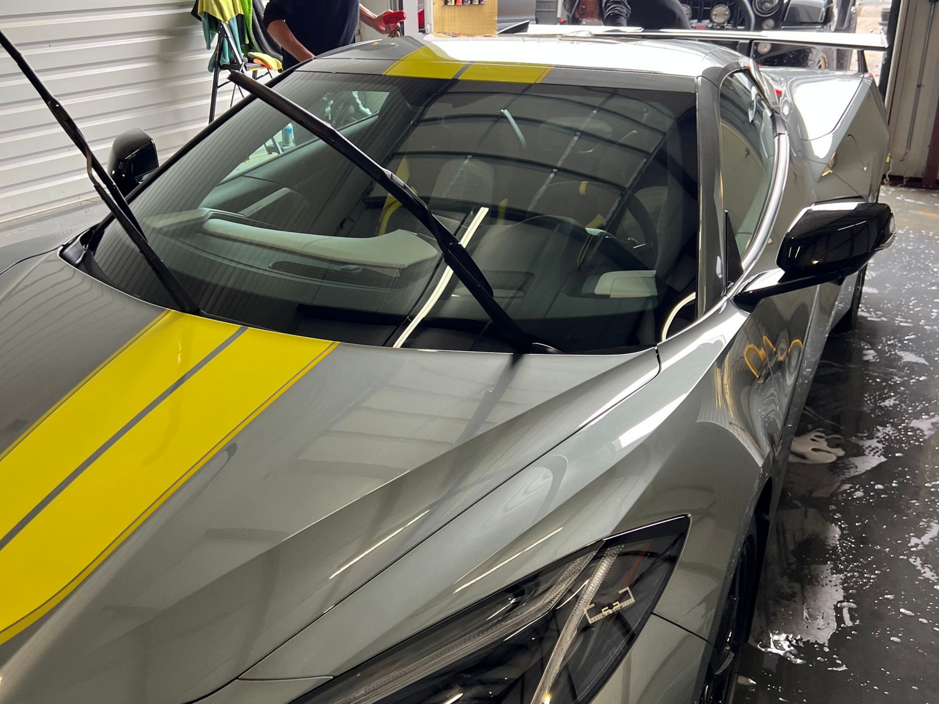 Gray sports car with yellow stripes being washed; wipers up.
