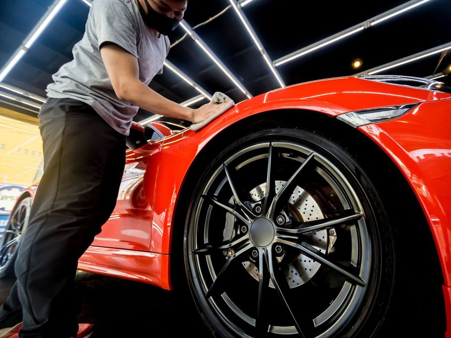 Technician wiping down a red sports car's fender during ceramic coating application