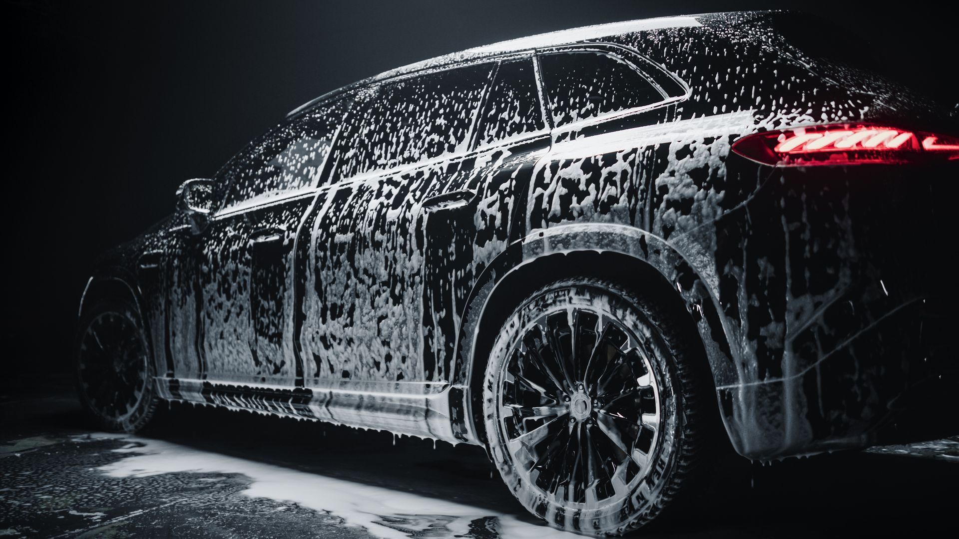 Black SUV covered in white foam, illuminated with red taillights.