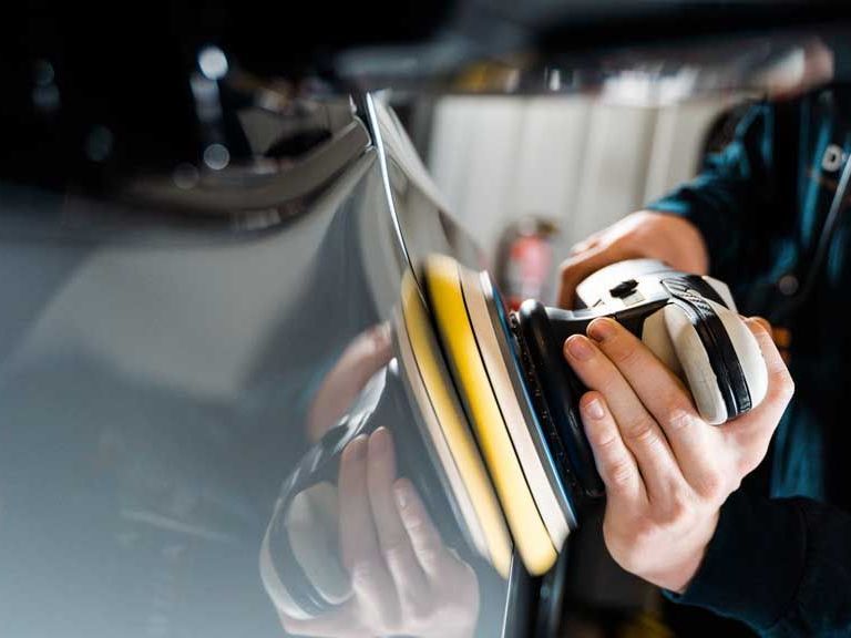 Person polishing a gray car with a power buffer.