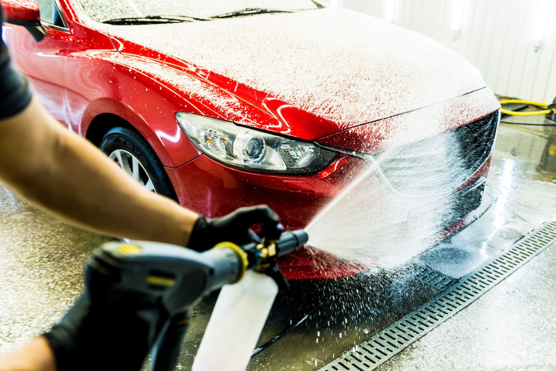 A person using a foam cannon to wash a red car in a car wash bay.