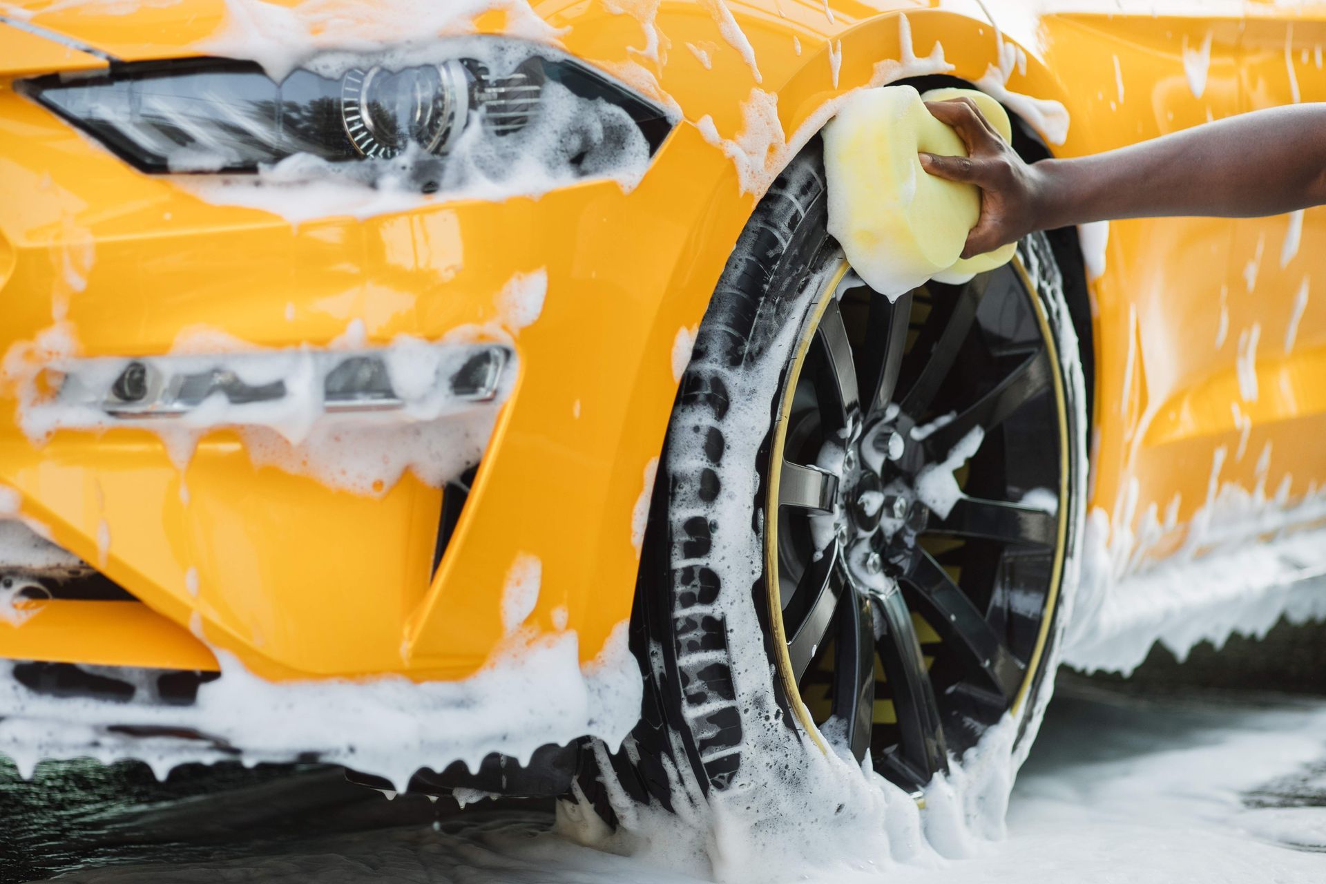 Yellow car being washed, person using a sponge.