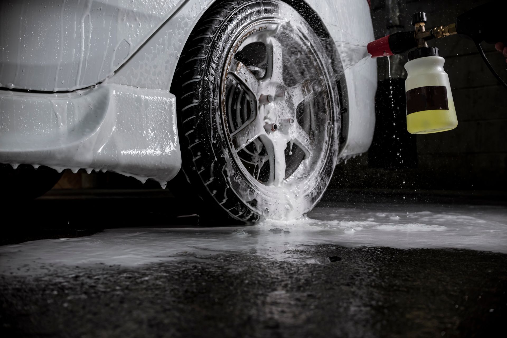 Car wheel being sprayed with foamy soap in a dark garage.
