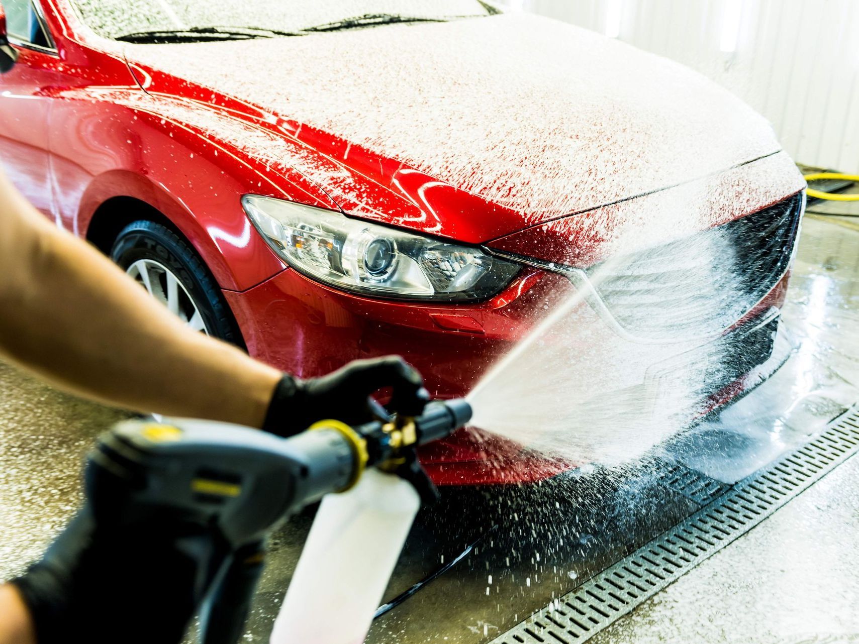 Person washing a red car with foamy soap in a car wash.