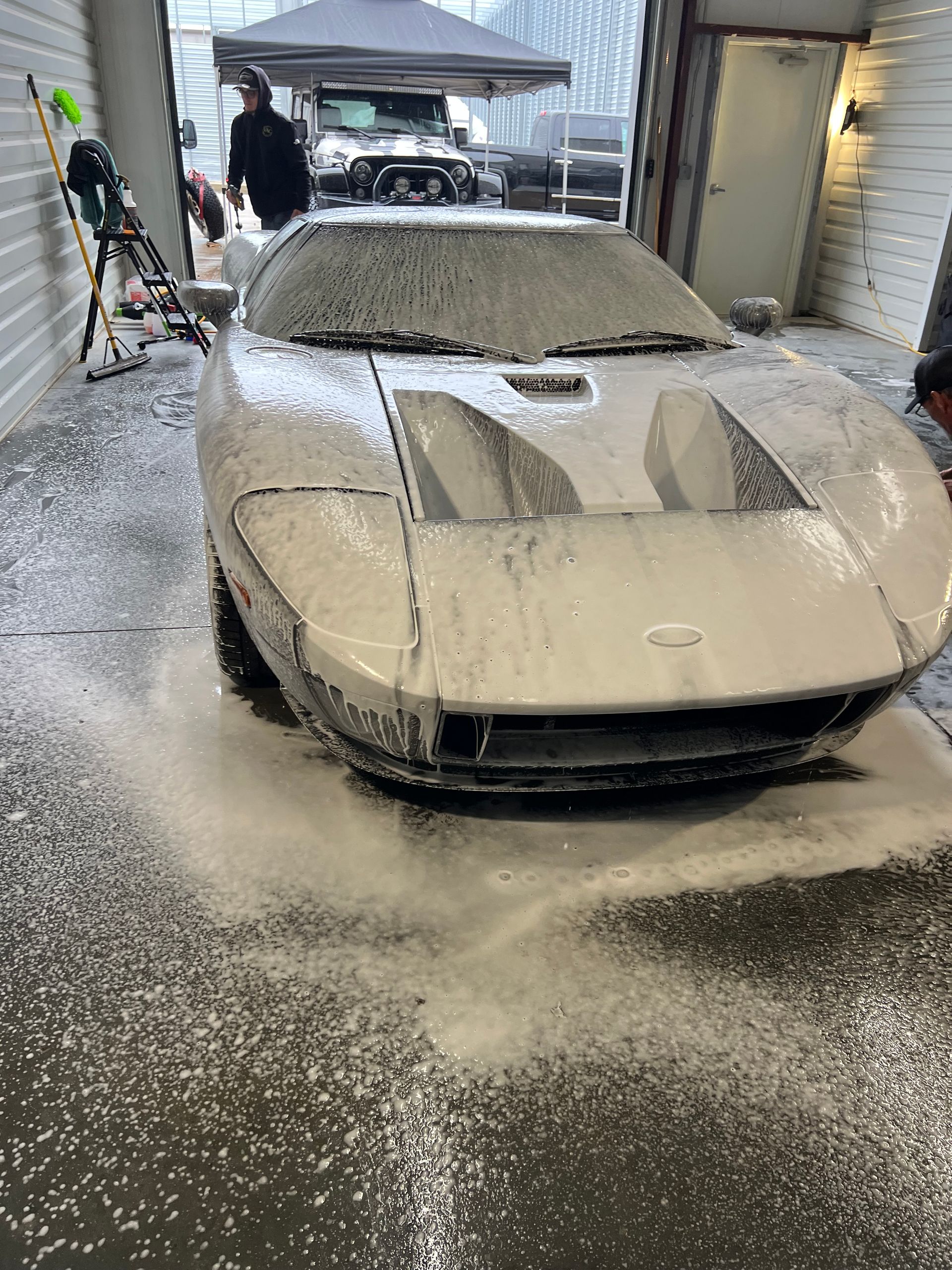 White Ford GT sports car covered in foamy soap suds, being washed in a garage.