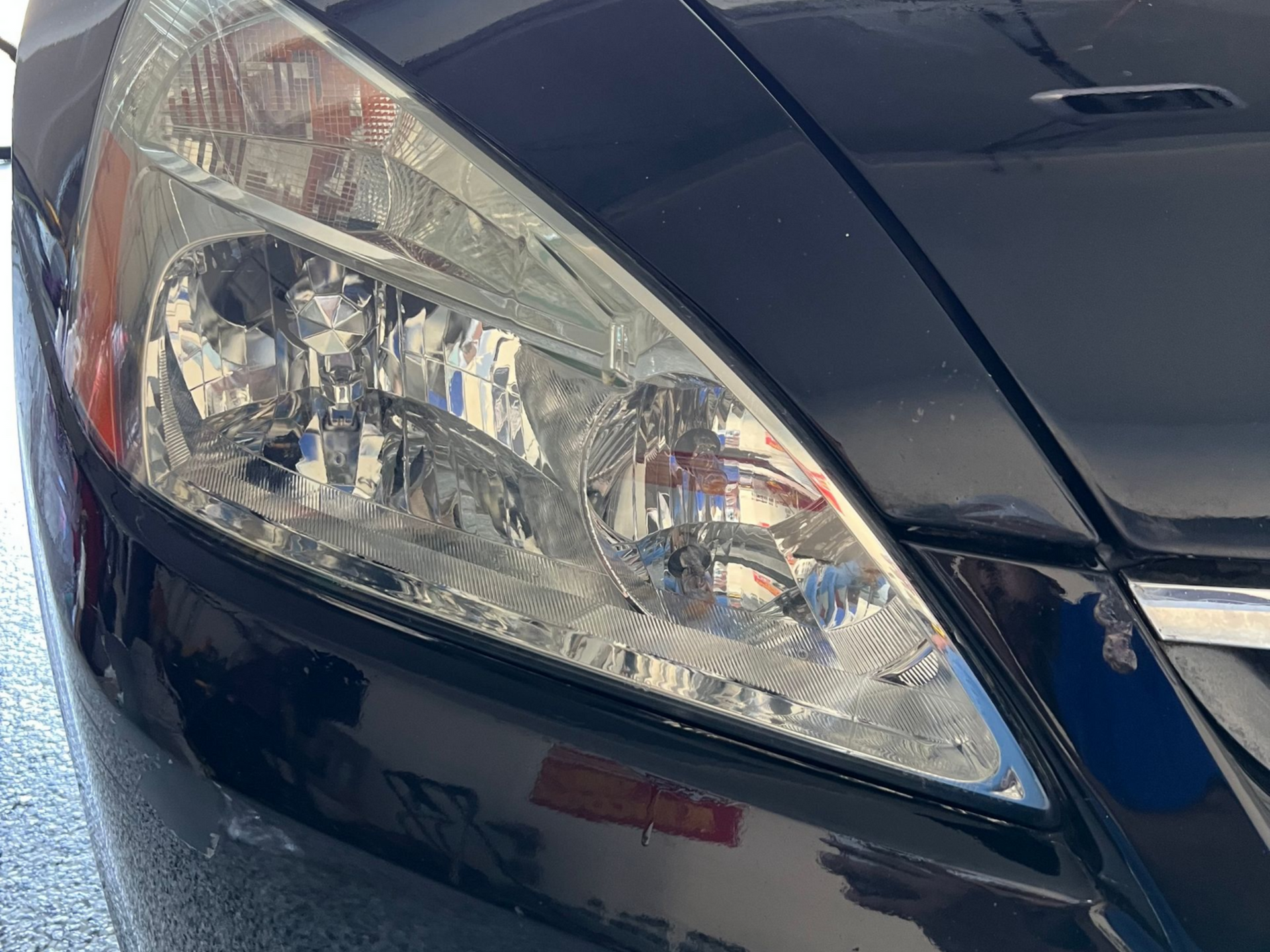 Black car headlight, bright and clear, reflecting light.